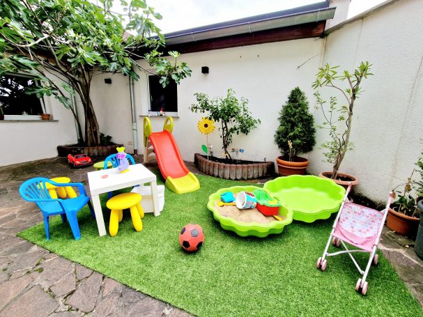 Spielplatz im Freien mit Rutsche, Sandkasten, Spielzeug und Kindermöbeln.